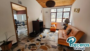 A spacious living area with a large window, a brown leather sofa, a wooden ceiling, and a mosaic floor. - PARCEROS GROUP-VACATION ROOM FOR COUPLES, FLOOR 1, PEREIRA (pereira)