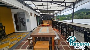 A covered outdoor dining area with a long table and benches, a view of a green landscape, and a sign for 'Parcero Group'. - PARCEROS GROUP-VACATION ROOM FOR COUPLES, FLOOR 1, PEREIRA (pereira)
