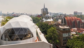 A dome-shaped building with a geometric exterior, adjacent to a traditional building with a dome and spire, amidst a cityscape with various buildings.