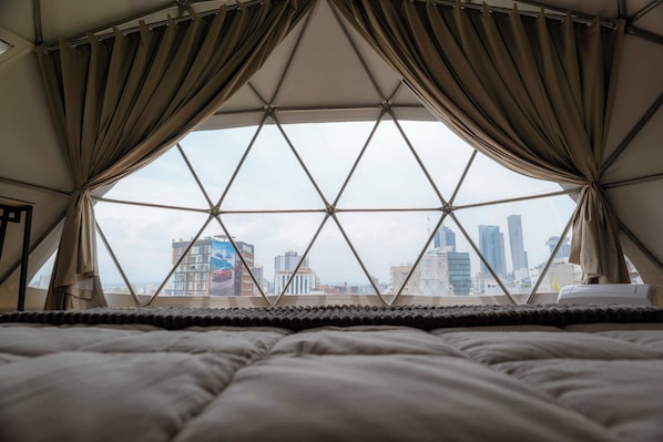 Una cama con vista a un paisaje urbano a través de una estructura de ventana geométrica.