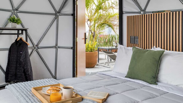A hotel room with a bed, a tray with breakfast items, a hanging coat, and a view of the outdoors. - Umbral | Sky Domes in Roma Norte (Tonali) (Ciudad de México)