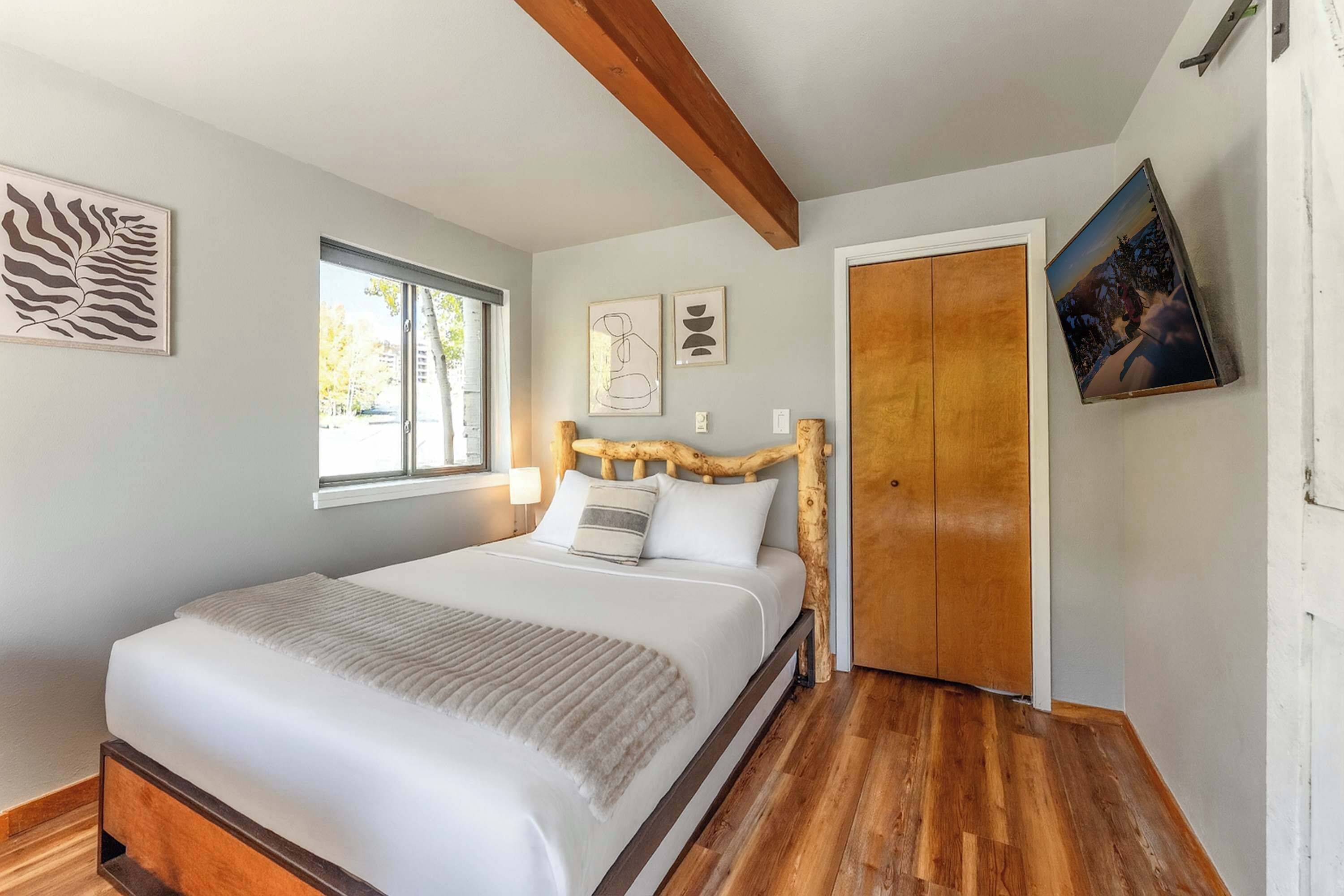 Une chambre à coucher avec une tête de lit en bois, une grande fenêtre et une porte.