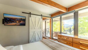 Ein Schlafzimmer mit einem Bett, einer Holzkommode, einer Schiebetür im Scheunenstil und einem großen Fenster mit Blick ins Freie.