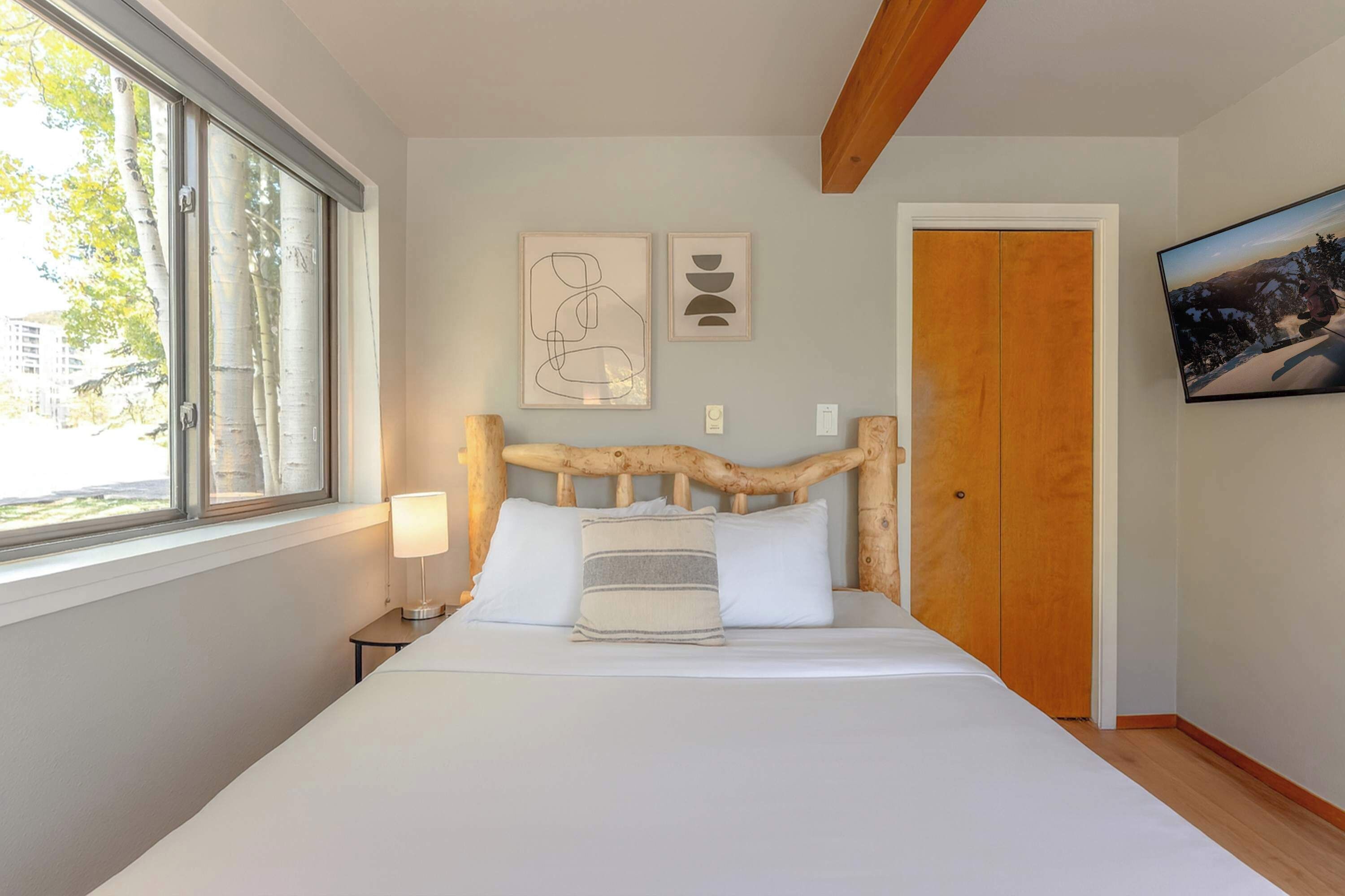 Un dormitorio con cabecera de madera, cama con ropa de cama blanca, lámpara de noche y una obra de arte en la pared.