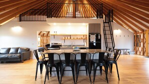 Um amplo loft com pé direito alto, área de jantar com mesa grande e cadeiras, cozinha equipada com eletrodomésticos modernos e um espaço de estar aconchegante com um sofá.