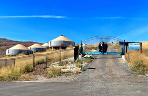 A gated entrance to a yurt settlement with a clear sky and dry grass. - OsoBlu Yurts Group Booking (Garden City)