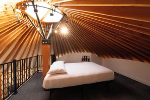 A bedroom with a sloped ceiling, a bed, a nightstand, and a desk with a chair. - OsoBlu Yurts Group Booking (Garden City)