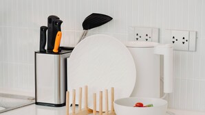 Una encimera de cocina con un plato blanco, un bol con una cereza, un bloque de cuchillos y una espátula.