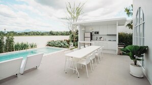 Una cocina exterior moderna con piscina, mobiliario blanco y vistas al paisaje.