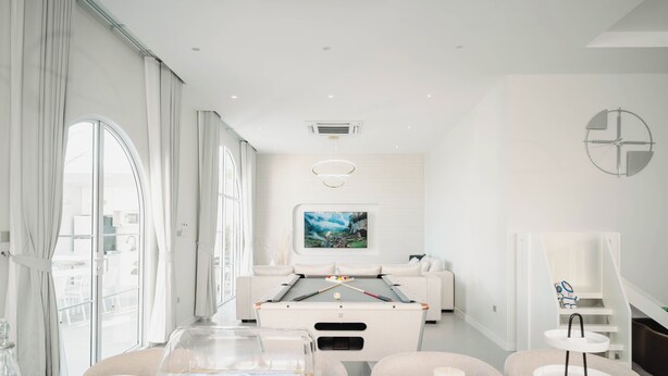Una habitación moderna y bien iluminada con mesa de billar, asientos cómodos y un amplio ventanal con vistas al exterior.