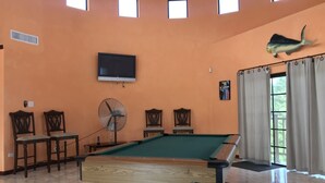 Ein Billardtisch in einem Raum mit orangefarbenen Wänden, einem Wandfernseher und einer Fischdekoration.