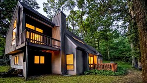 A modern two-story house with a balcony, surrounded by trees.