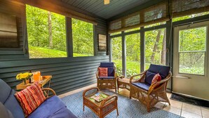 A cozy room with a large window overlooking a lush garden, wicker furniture, and a small table with a magazine.