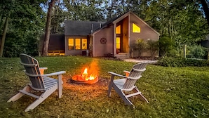 A cozy cabin with a fire pit in the center, surrounded by two Adirondack chairs.