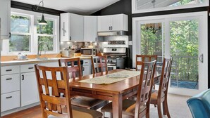 A modern kitchen with white cabinets, a wooden dining table, and a view of the outdoors. - Cozy cabin w/ Screened porch & BBQ (Hedgesville)