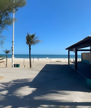 Una spiaggia con un'area salotto coperta, cielo sereno e mare calmo.