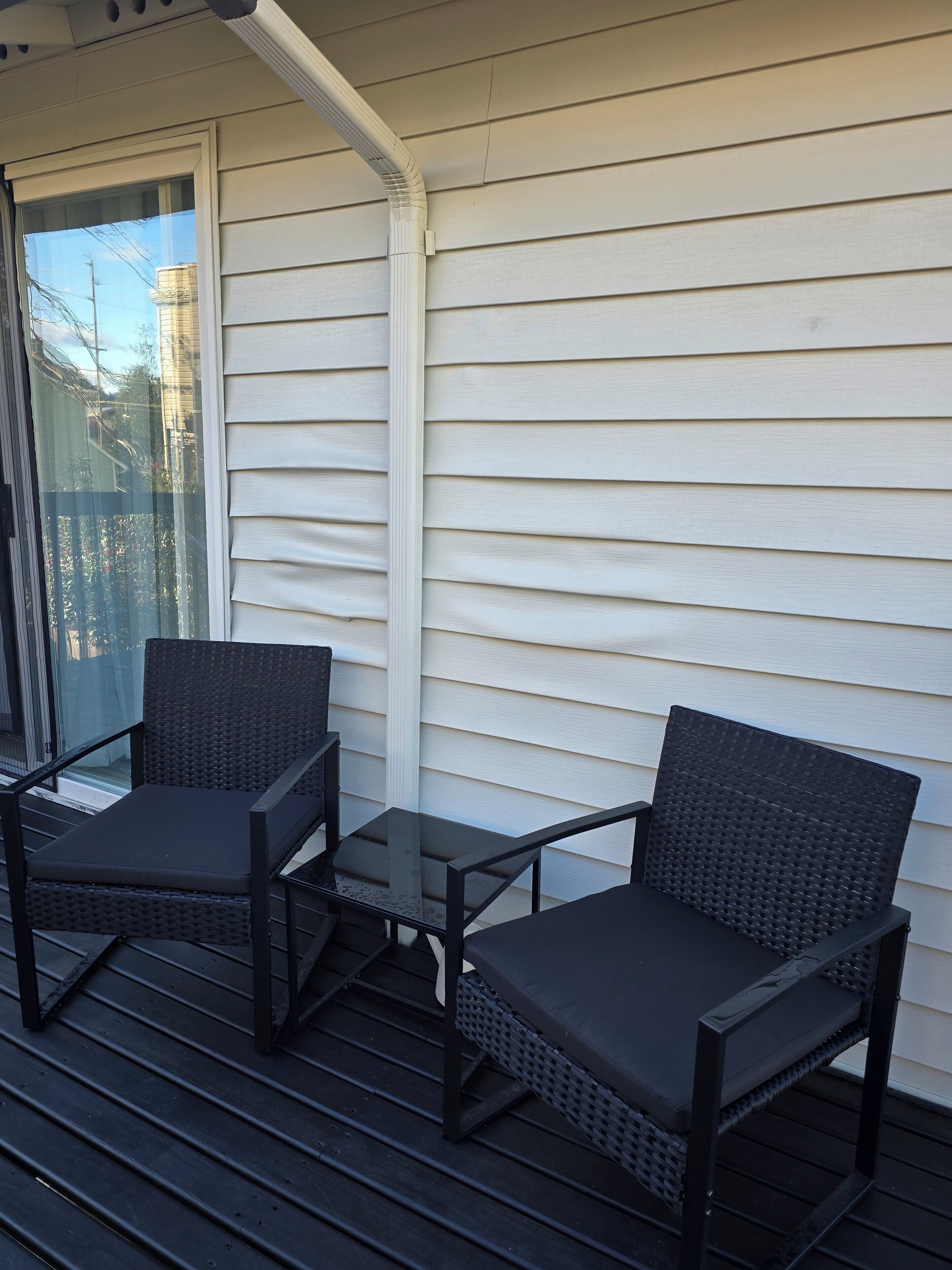 A covered outdoor seating area with two chairs and a small table, adjacent to a sliding glass door.
