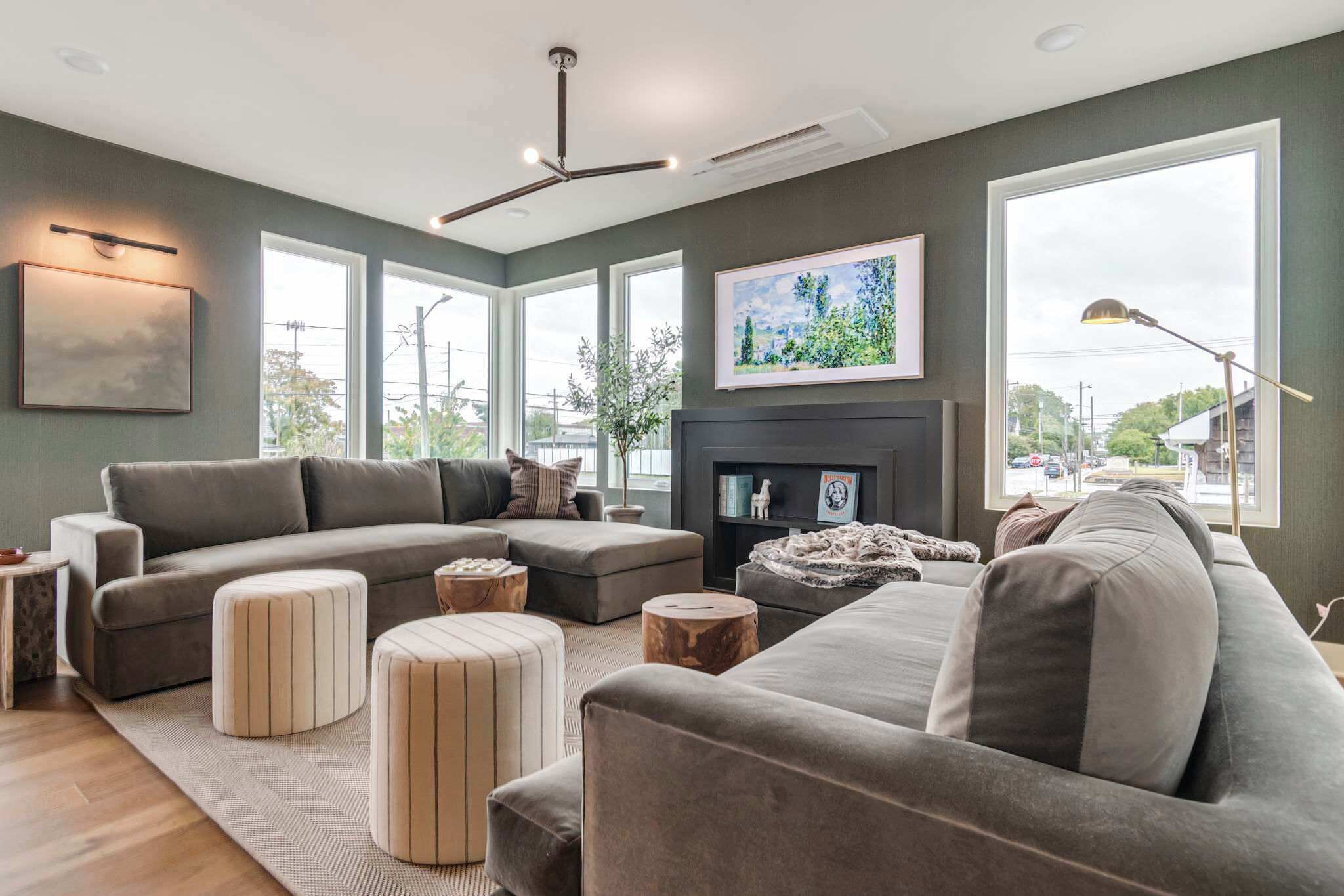 A modern living room with a sectional sofa, ottomans, a fireplace, and large windows offering a view of the outdoors.