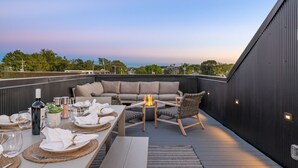 Terraço no telhado com uma mesa de jantar para quatro pessoas, um sofá e uma pequena lareira.