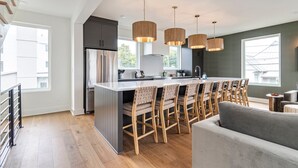Cozinha moderna com ilha central, cadeiras de madeira e luminárias pendentes.