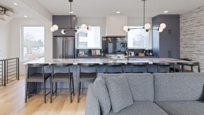 Une cuisine moderne avec un îlot central, des tabourets de bar et un canapé gris au premier plan.