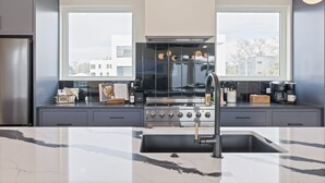 Une cuisine moderne dotée d’un grand îlot central, d’appareils électroménagers en acier inoxydable et offrant une vue sur la ville grâce à de grandes fenêtres.