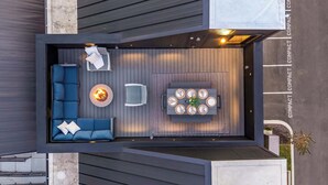 Un petit patio extérieur comprenant un canapé bleu, une table ronde avec des assiettes, un foyer et une chaise.