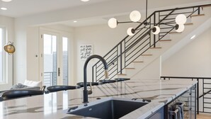 Une cuisine moderne dotée d’un grand îlot central, d’un robinet noir et de luminaires suspendus.