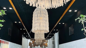 Een modern interieur met een centrale doorgang, decoratieve houten franjes aan het plafond en potplanten langs de muren.