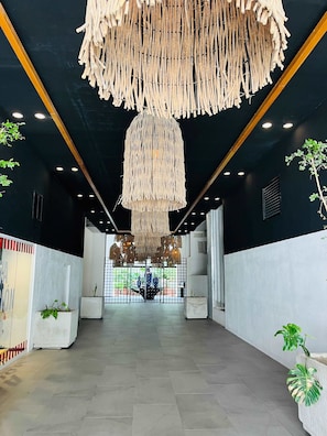 A modern interior with a central walkway, decorative wooden fringes hanging from the ceiling, and potted plants along the walls.