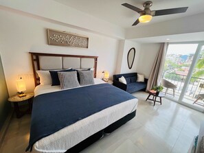 Een moderne hotelkamer met een groot bed, een plafondventilator, uitzicht op de stad en een balkon met een stoel.