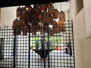 A room with a black metal grid partition, a hanging woven light fixture, and a view of an outdoor area with potted plants. - Life Bucerías: Modern Studio Near the Beach (Bucerías)