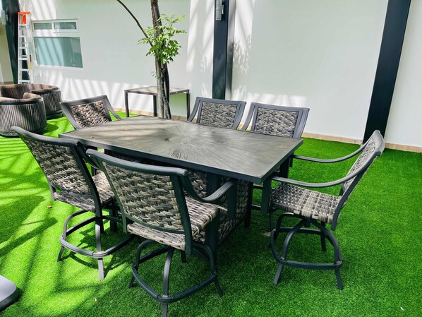 Une table rectangulaire pour l’extérieur, accompagnée de six chaises, le tout entouré de gazon artificiel.
