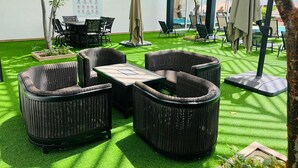 Een terras met rieten meubilair, kunstgras en parasols.