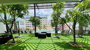 Een terras buiten met kunstgras, ligbedden en potplanten.