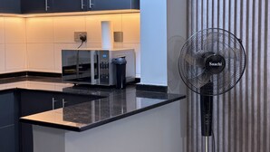 Une cuisine moderne avec un plan de travail noir, un four à micro-ondes et un ventilateur Saachi.