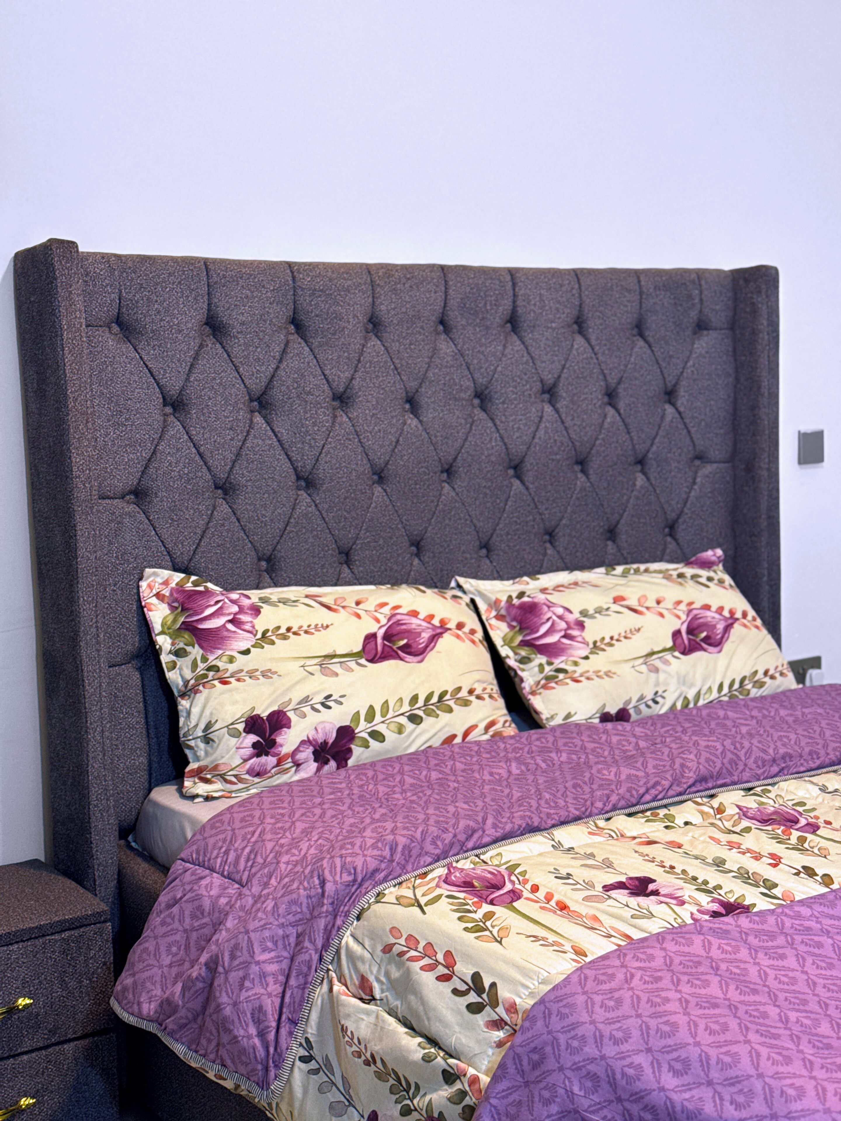 A bed with a tufted headboard, floral-patterned pillows, and a purple bedspread.
