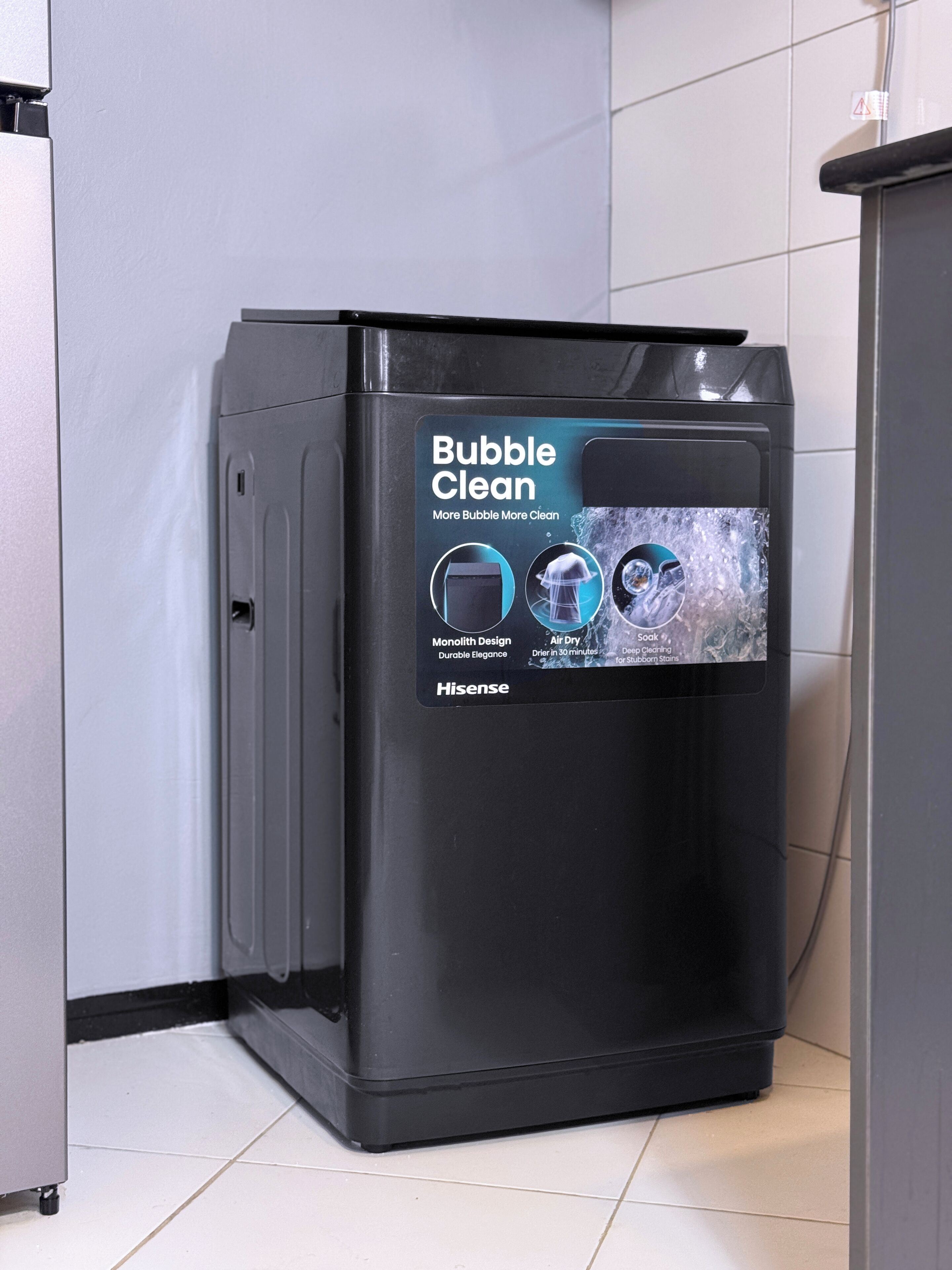 A black Hisense bubble cleaner in a corner of a room with white tiled walls and floor.