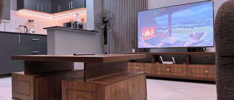 A modern kitchen with dark cabinets, a built-in TV, and a wooden coffee table with drawers.