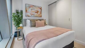 Une chambre moderne avec un grand lit, une table de chevet avec une lampe, une plante en pot et un tableau abstrait accroché au mur.