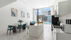 A modern kitchen with a built-in oven, a dining area with teal chairs, and a view of a swimming pool. - Unique Townhouse Pool Slide Access (Bophut)