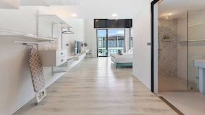 A modern hotel room with a minimalist design, featuring a large bed, a seating area, and a glass-enclosed shower. - Unique Townhouse Pool Slide Access (Bophut)