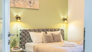 Un dormitorio con cabecera capitonada, dos lámparas de noche, una mesita de noche con una planta y una cama bien hecha con toallas.
