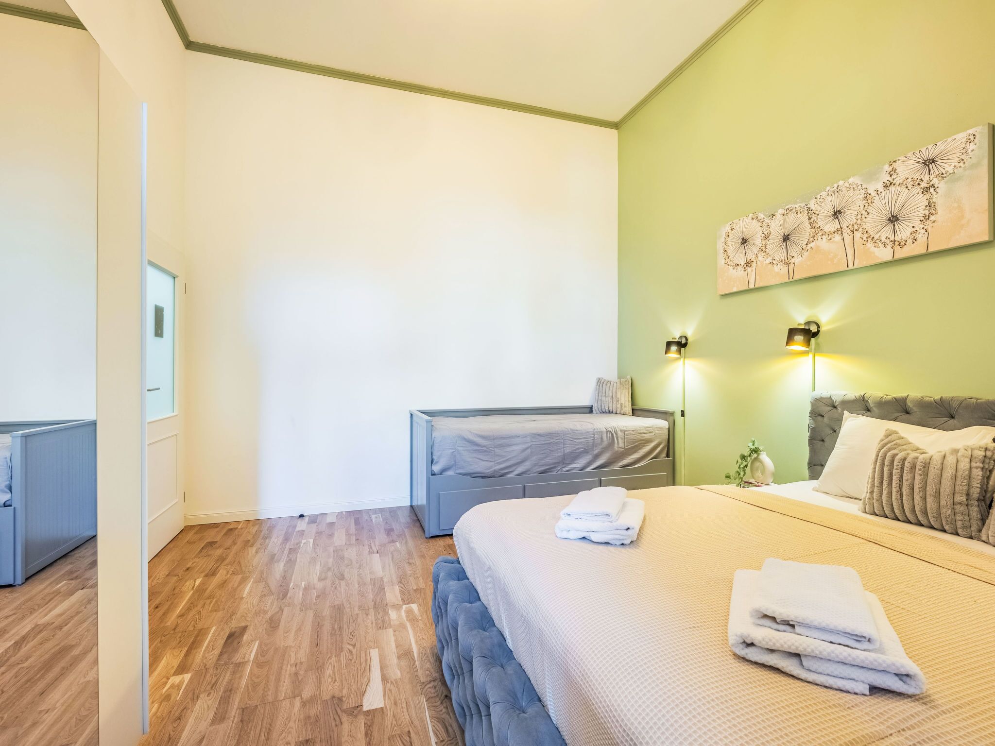 Una camera da letto con un letto grande, un letto più piccolo, un comodino e una lampada a parete.