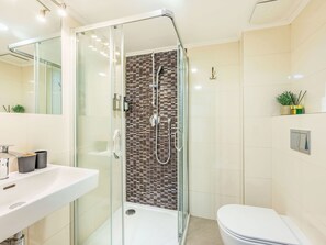 Un baño moderno con ducha de vidrio, lavamanos blanco y retrete.