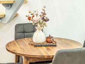 Una mesa redonda de madera con un jarrón blanco de flores secas y una pequeña maceta de cerámica.