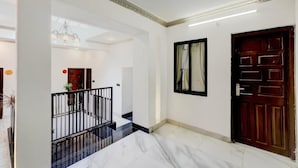 Ένας ευρύχωρος διάδρομος με μαρμάρινο δάπεδο, μια ξύλινη πόρτα και έναν καθρέφτη με μαύρο πλαίσιο.