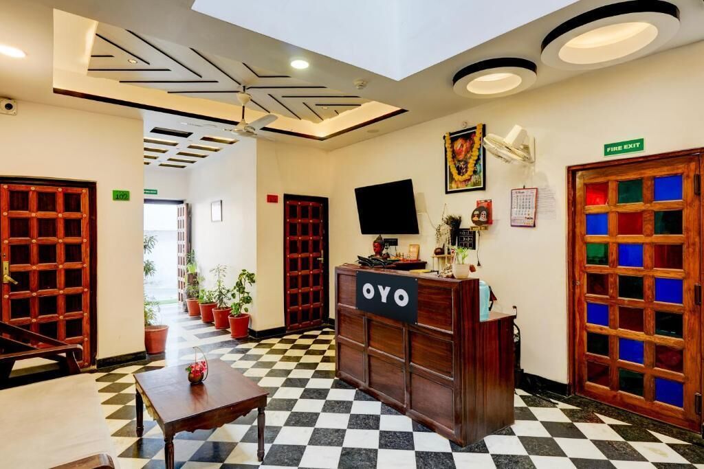 A reception area with a checkered floor, a reception desk labeled "OYO," a ceiling fan, a fire exit sign, and a television on the wall.