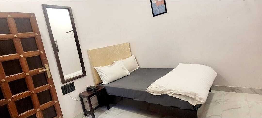 A bedroom with a bed, a bedside table, a mirror, and a door.