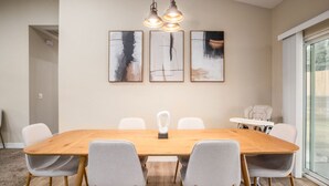 A modern dining room with a wooden table, six grey chairs, and three abstract paintings on the wall. - Yosemite/Bass Lake Oasis – Modern Furnishings, Hot Tub, Game Room, EV Plug, BBQ & Fire Pit, Pet‑Friendly | Sleeps 19+ | 5 Mins to Downtown (Oakhurst)